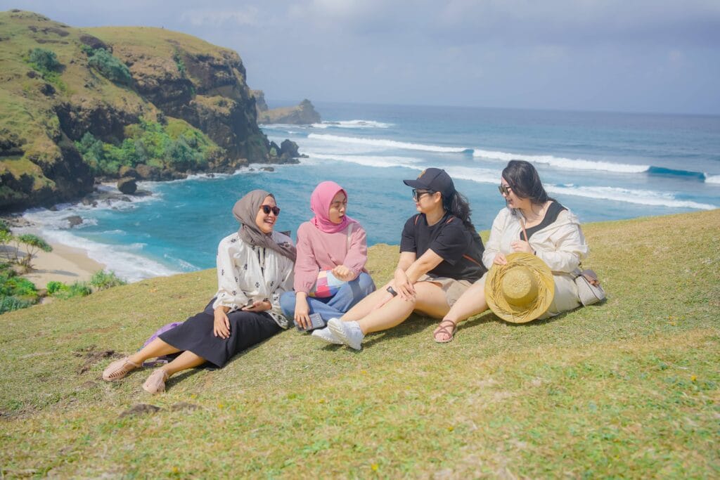 Empat orang wanita sedang duduk santai di atas Bukit Merese, Lombok, sambil menikmati pemandangan laut biru.