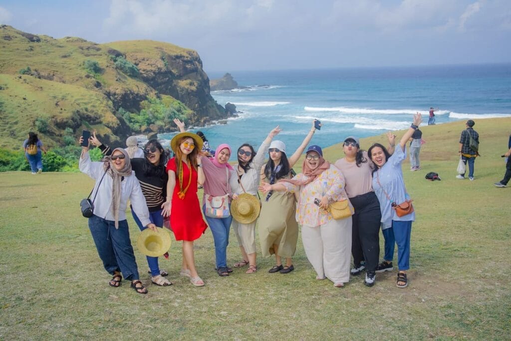 Sekelompok wisatawan wanita berpose ceria di puncak Bukit Merese dengan latar belakang pemandangan pantai Lombok Selatan.