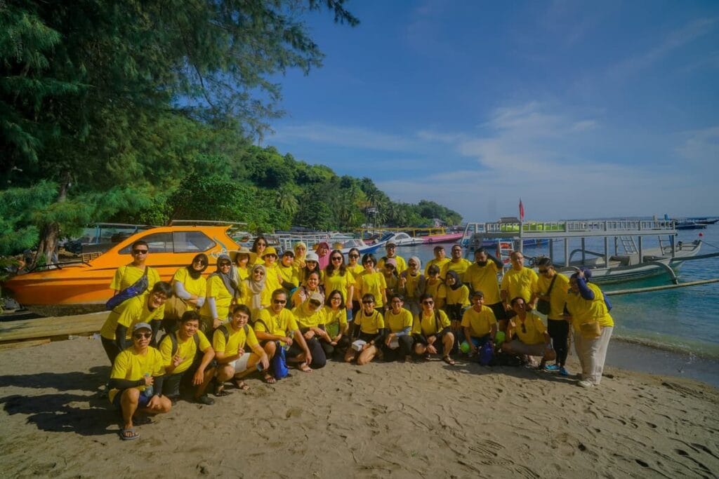 Sebuah rombongan besar wisatawan mengenakan seragam kuning berfoto bersama di tepi pantai dekat pelabuhan di Lombok.