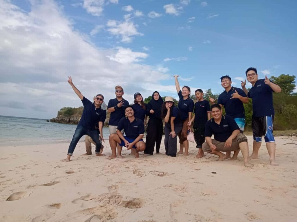 Peserta paket company outing bermain air dan berfoto ceria di Pantai Pink Lombok.