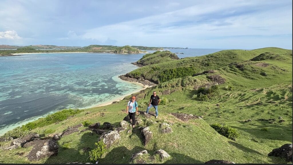Wisatawan Lombok Travelution berpose di puncak Bukit Merese dengan latar pemandangan Pantai Tanjung Aan dan Samudra Hindia yang memukau.
