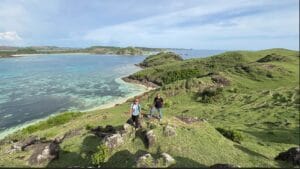 Wisatawan Lombok Travelution berpose di puncak Bukit Merese dengan latar pemandangan Pantai Tanjung Aan dan Samudra Hindia yang memukau.