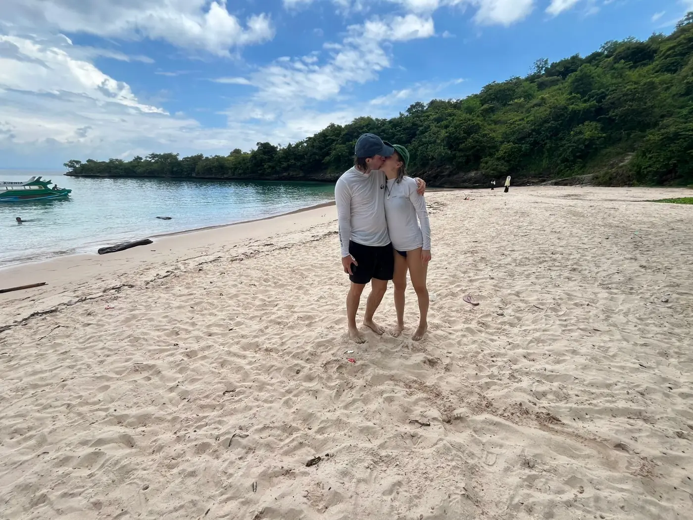 Couple on a quiet stretch of beach with a moored boat and green cliffs behind