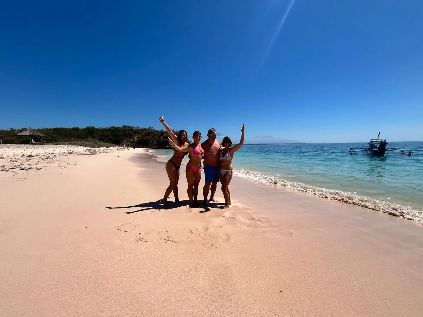 Family of four standing together on pink tinted sand beside calm water in Lombok