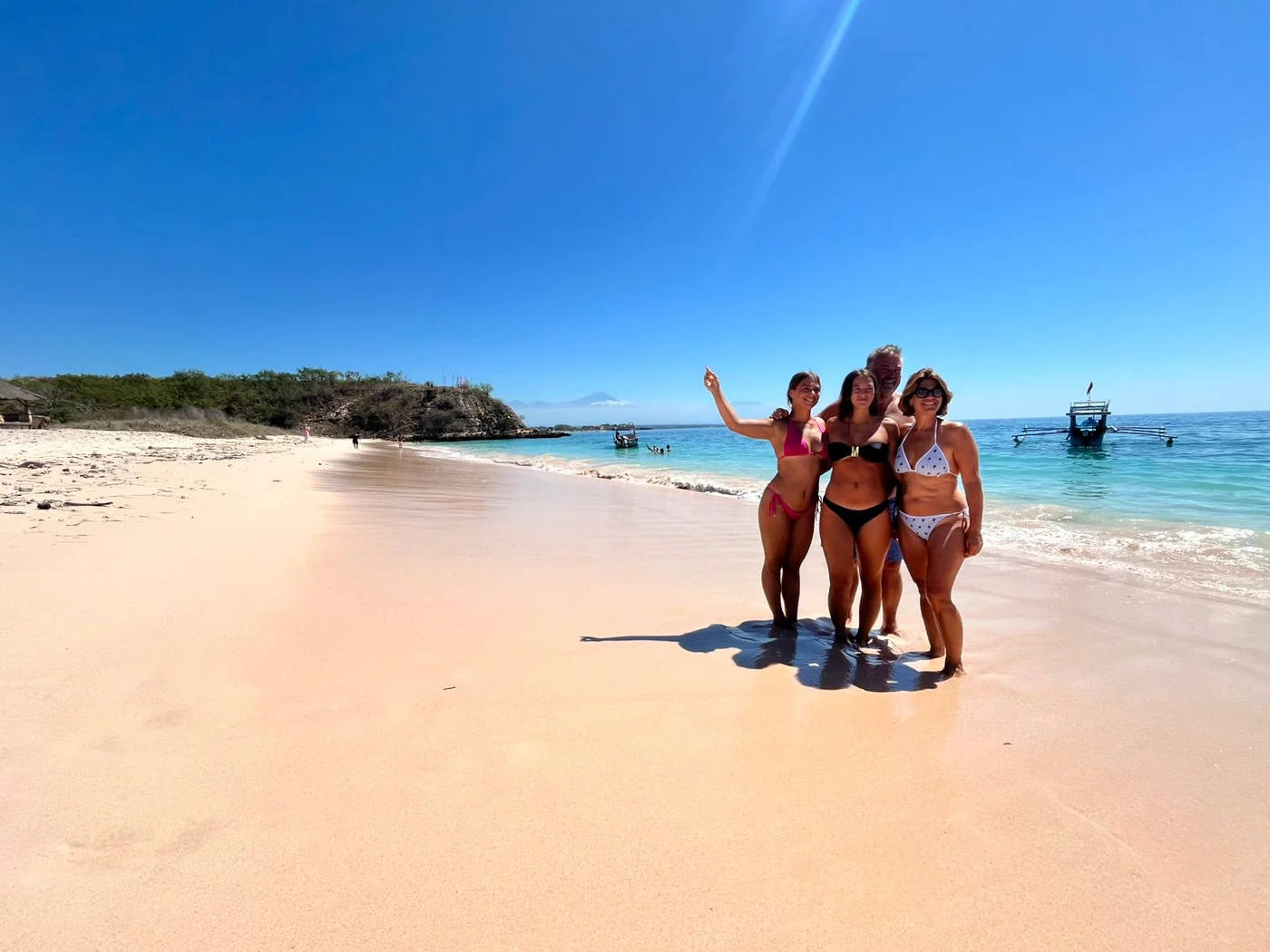 Family standing at the shoreline where pink sand meets clear blue water in Lombok